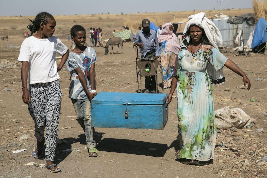 A scene from a refugee camp in Sudan showing three Tigrayans carrying a large metal case