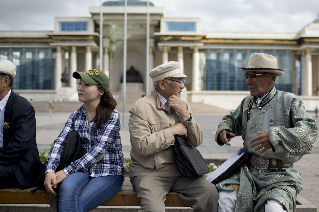 People sit on a bench in in front of the Mongolian parliament building, also known as the State Palace, on Sukhbaatar Square