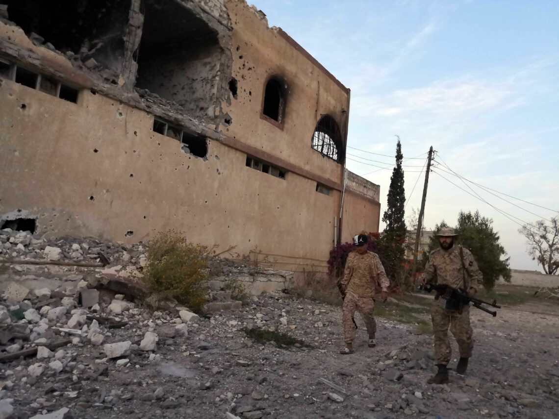 GNA soldiers walk by a damaged building in Tripoli, December 2019