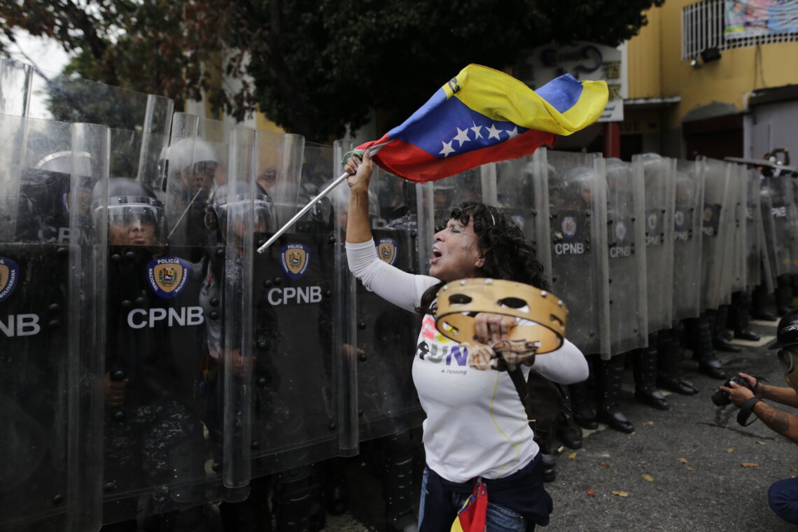 A protestor waves a Venezuelan flag near security forces in Caracas, Venezuela.
