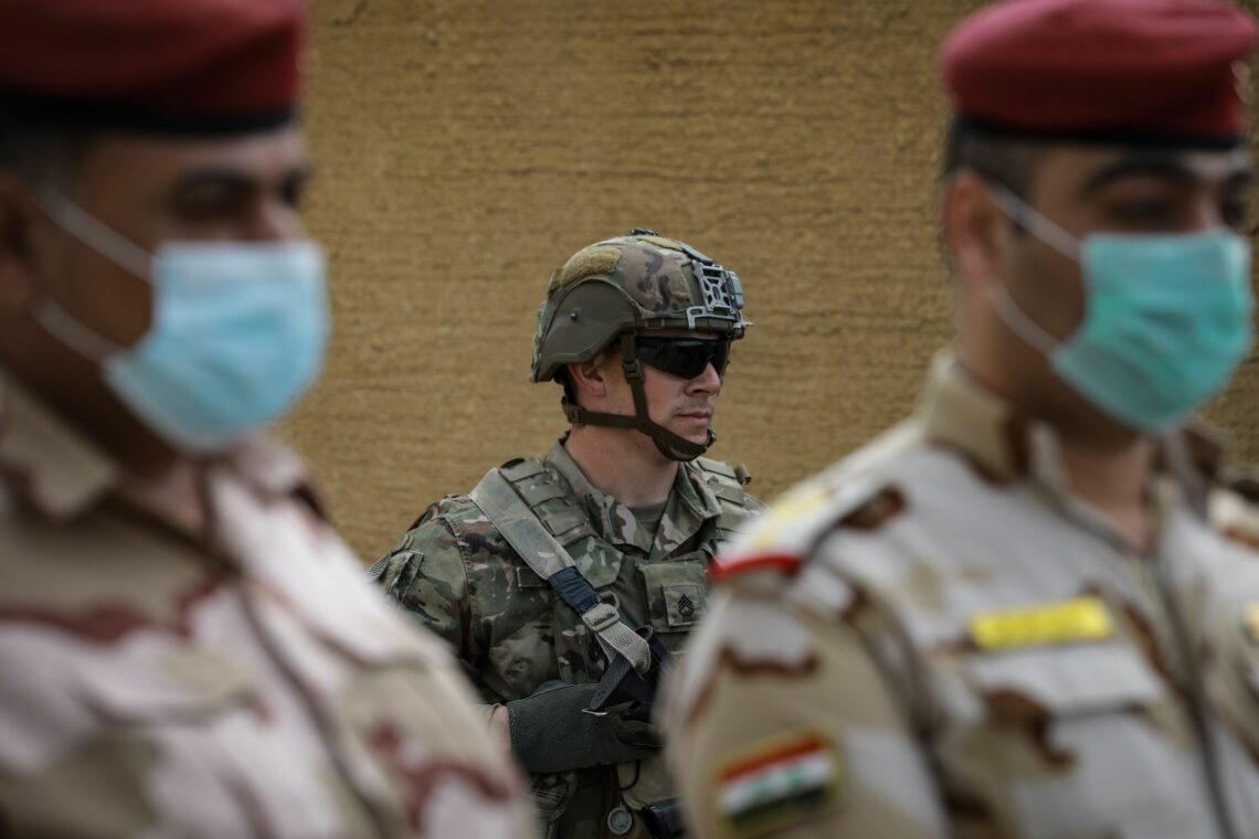 An American soldier stands behind Iraqi troops during the March, 2020 handover ceremony of the K1 Air Base near Kirkuk, Iraq.