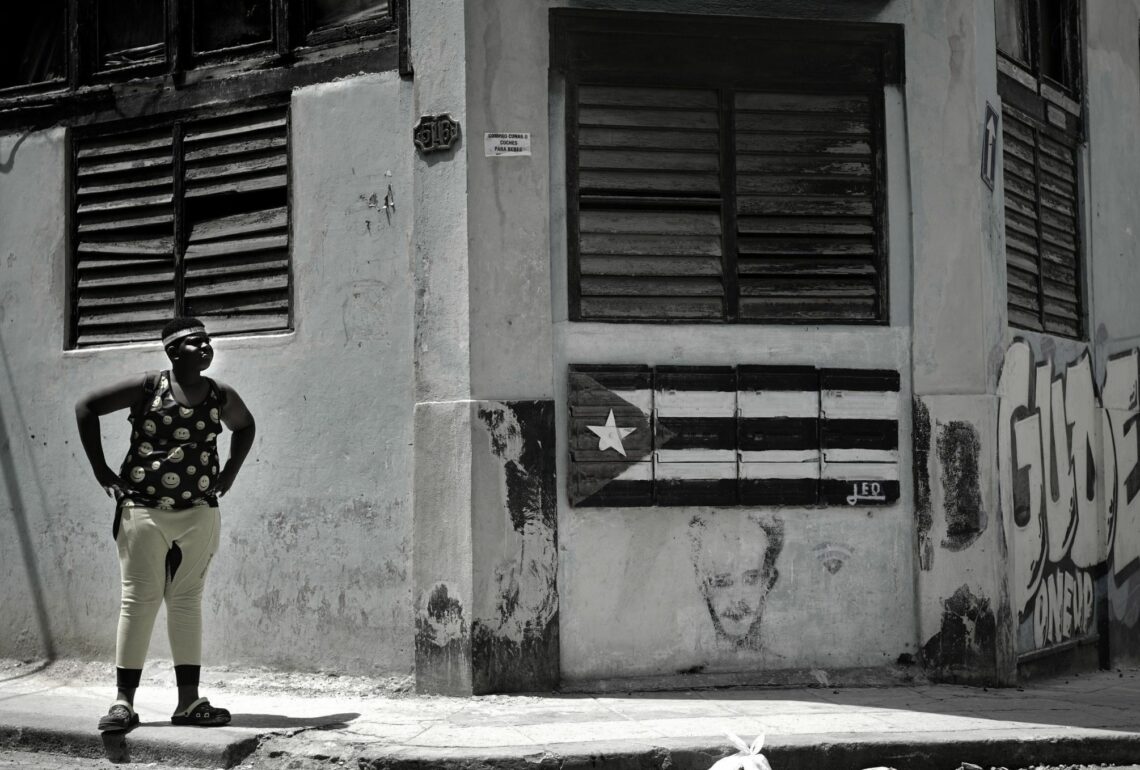 A young Cuban in tattered clothes stands next to a run-down building with the Cuban flag painted on it Cuba’s population