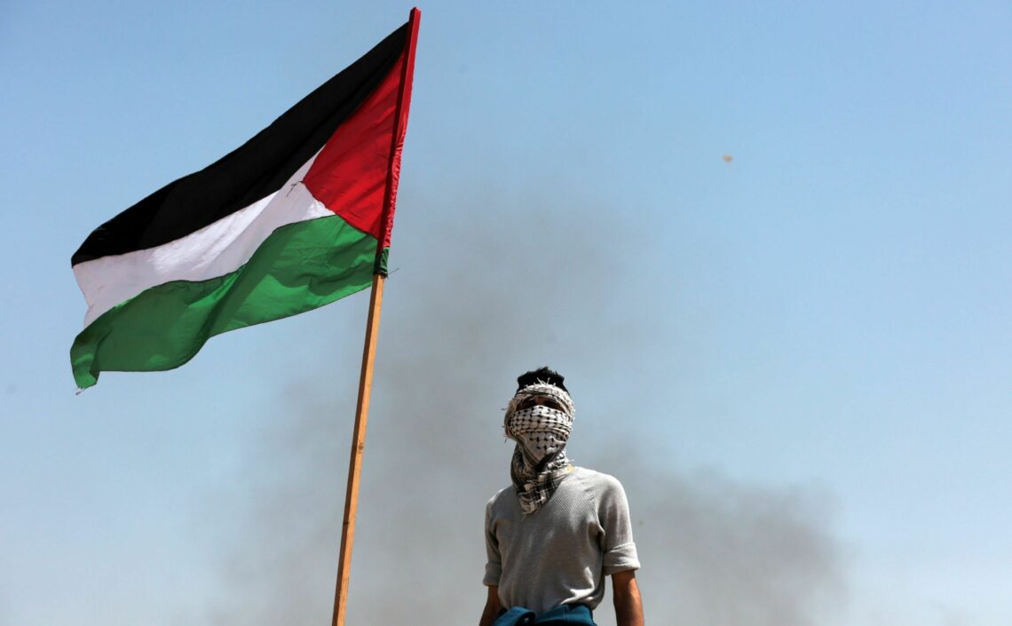 A protester stands next to a Palestinian flag at the Gaza-Israel border
