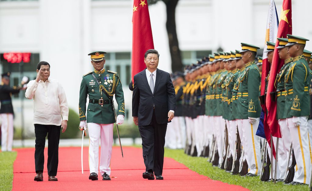 The leader of China walks in front of the honor guard in Manila, accompanied by the Philippine president and the guard commander