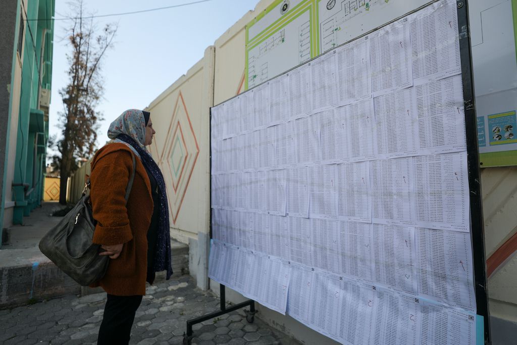 A picture of a Palestinian woman in Gaza looking at lists of eligible voters attached to a billboard stand