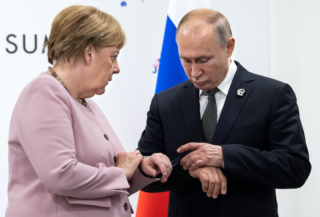 The leaders of Germany and Russia looking at their wristwatches as they chat during a G20 summit in Japan