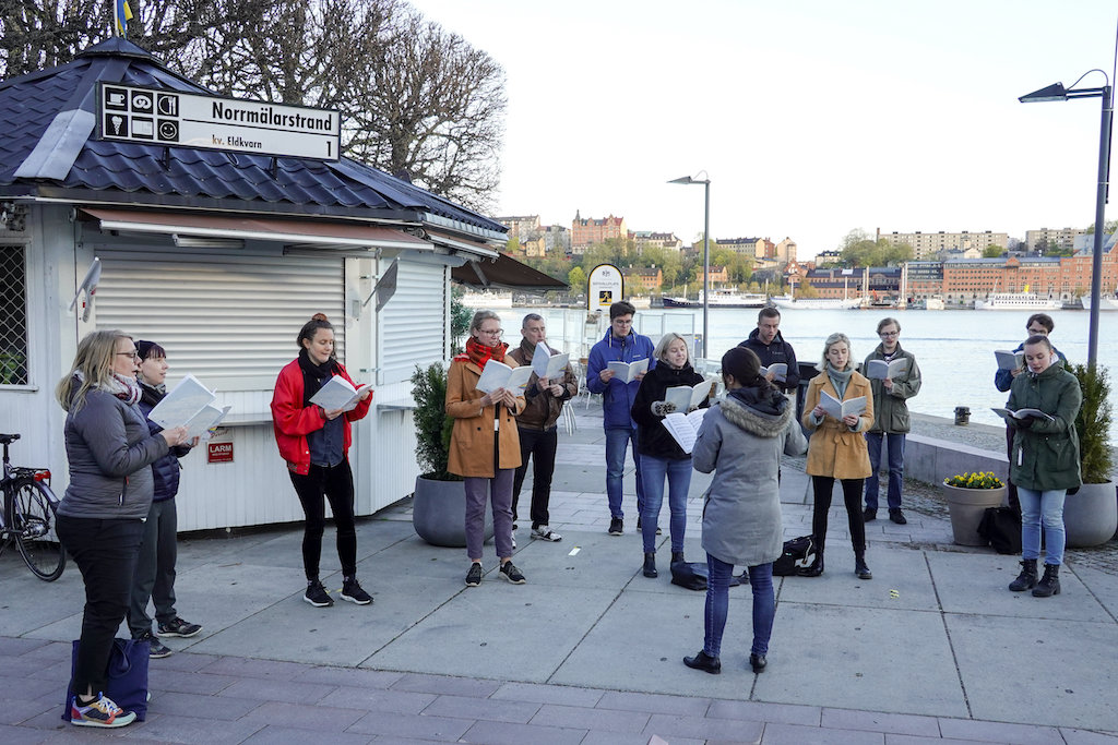 Picture of a group of young people singing outdoor near Stockholm’s City Hall.