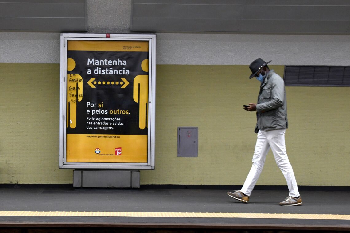 A masked man walks in a Lisbon subway station where a sign asks travelers to maintain social distancing