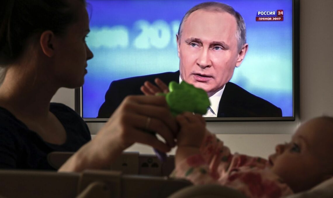 A woman and her baby watch Vladimir Putin on Russian television