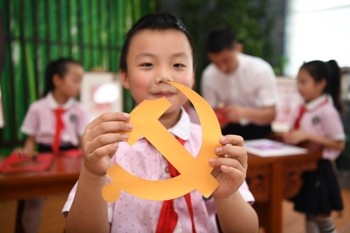 A picture of a Chinese primary school student holding a paper cutout of a hammer and sickle, the emblem of the Communist Party of China