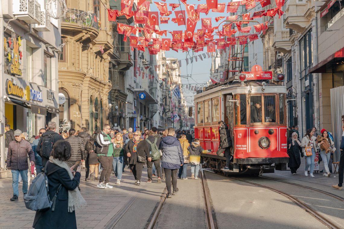 A red trolley with people on a street walking around.