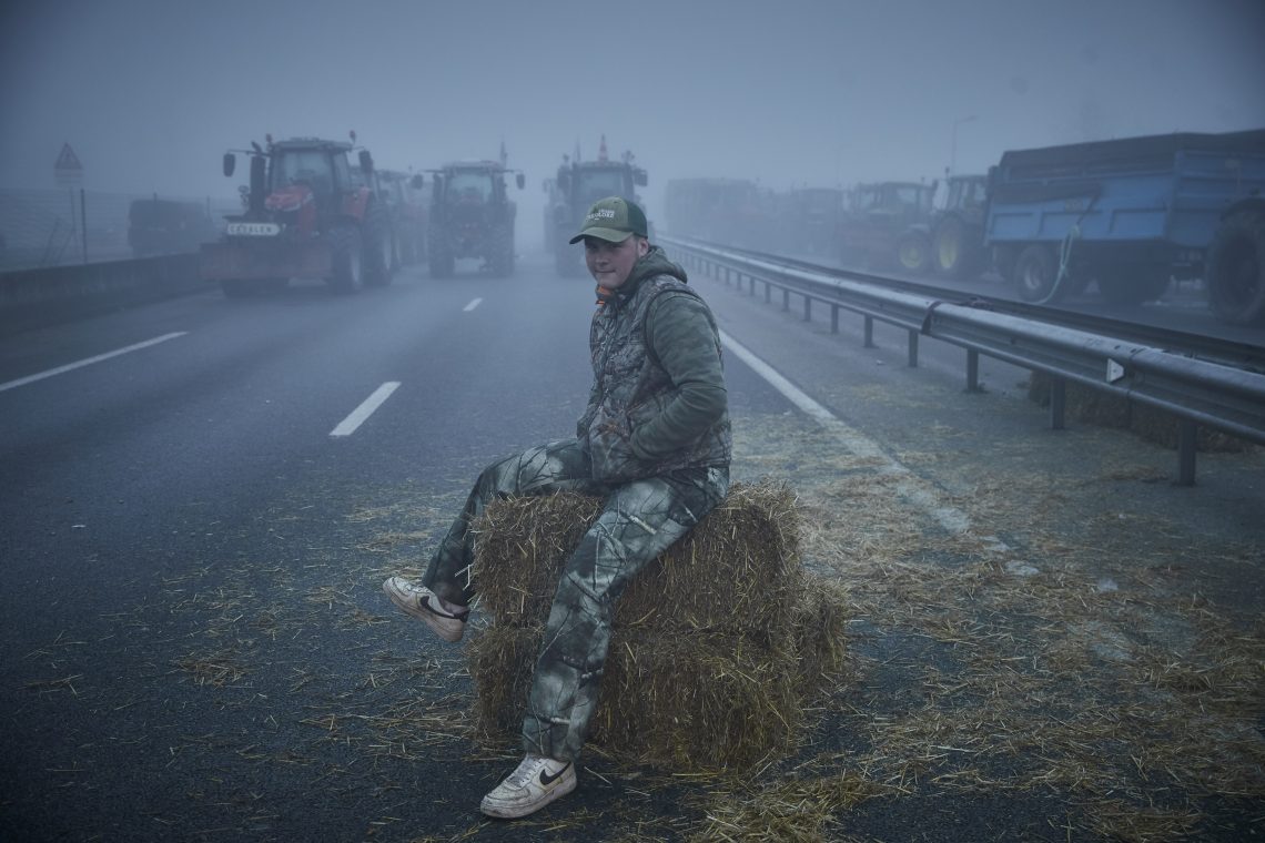 A protesting farmer sits on a bale of hay.