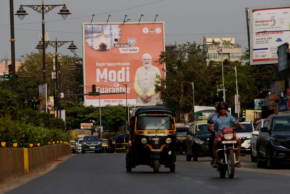 Commuters pass by Prime Minister Narendra Modi’s poster before the June 2024 general elections. Despite securing a third term, his Bharatiya Janata Party failed to achieve a parliamentary majority, indicating voter frustration with stagnant job creation and rising costs.