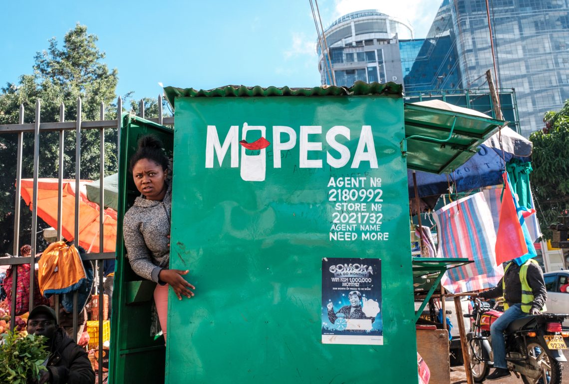 A woman looks out from a retail kiosk offering M-Pesa mobile money services in Nairobi, Kenya.